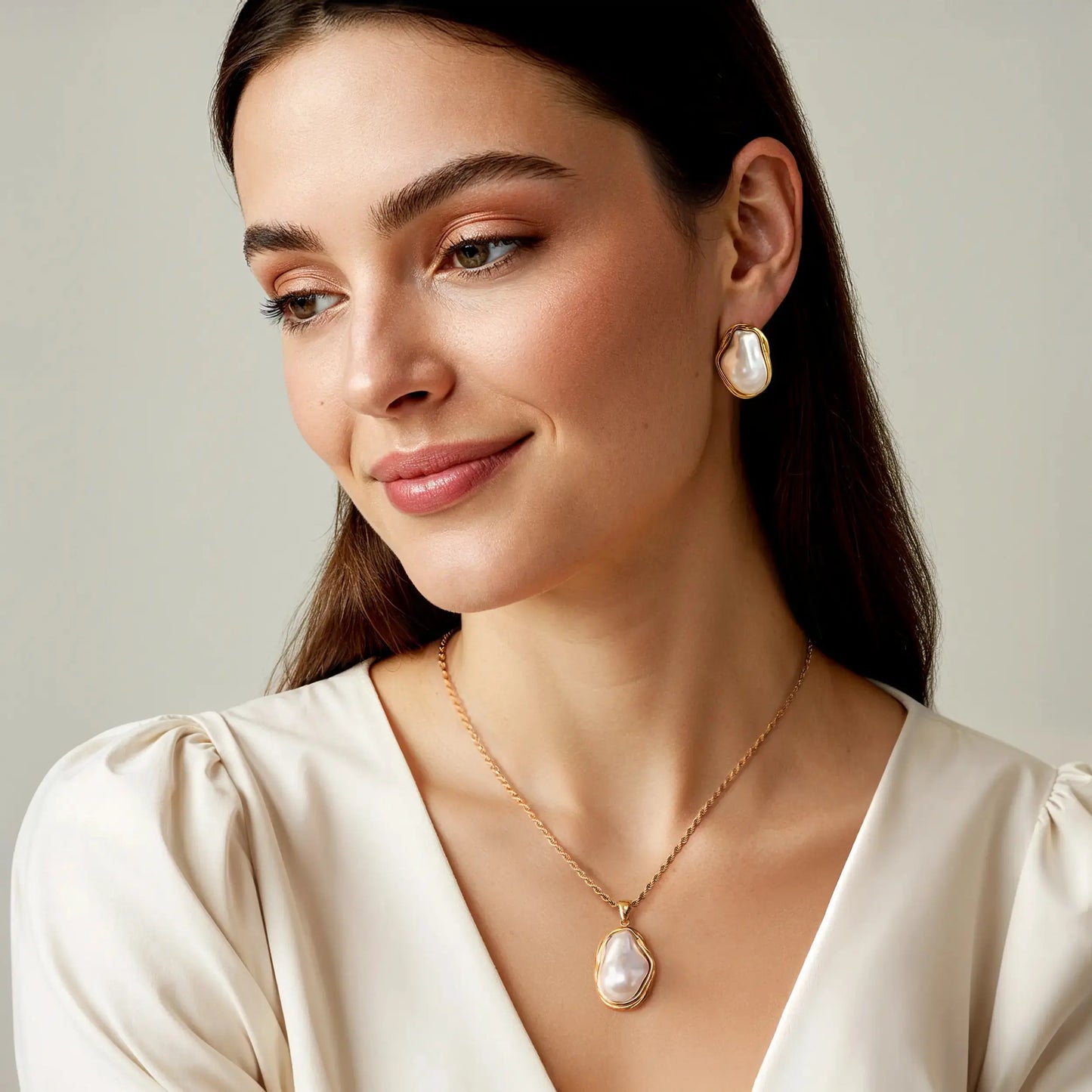 Woman wearing pearl earrings and necklace against a neutral background