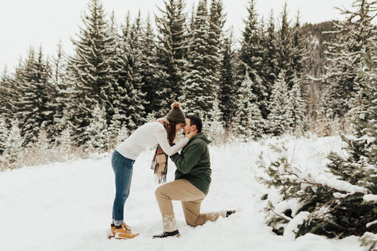 Man is staying on a knee in front of a woman in a snowing mountain