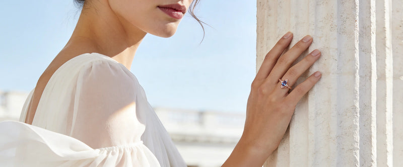 Woman wearing a ring with a blue gemstone against a bright sky.