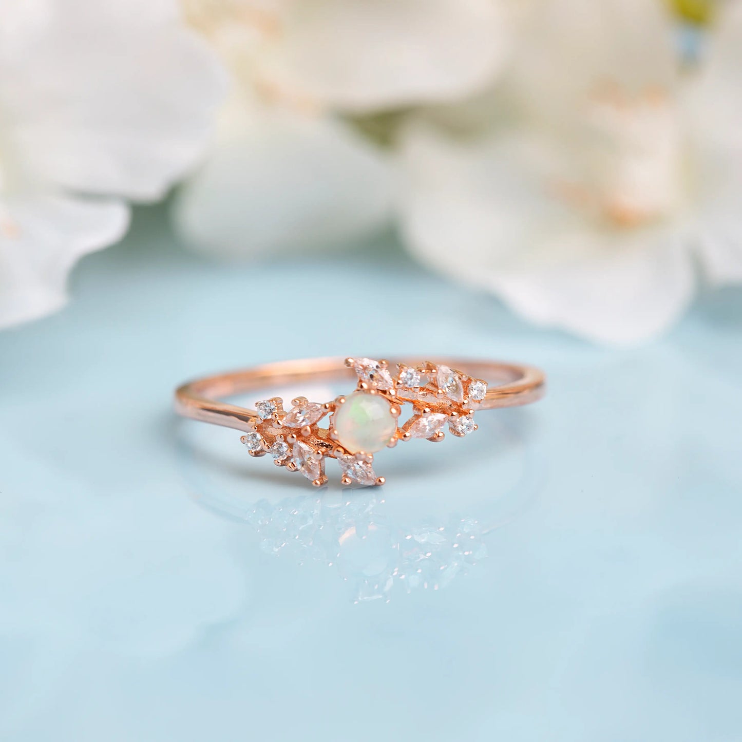 Rose gold ring with green gemstone on a light blue background with white flowers