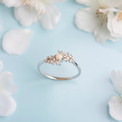 Gold ring with a central gemstone surrounded by white flowers on a light blue background
