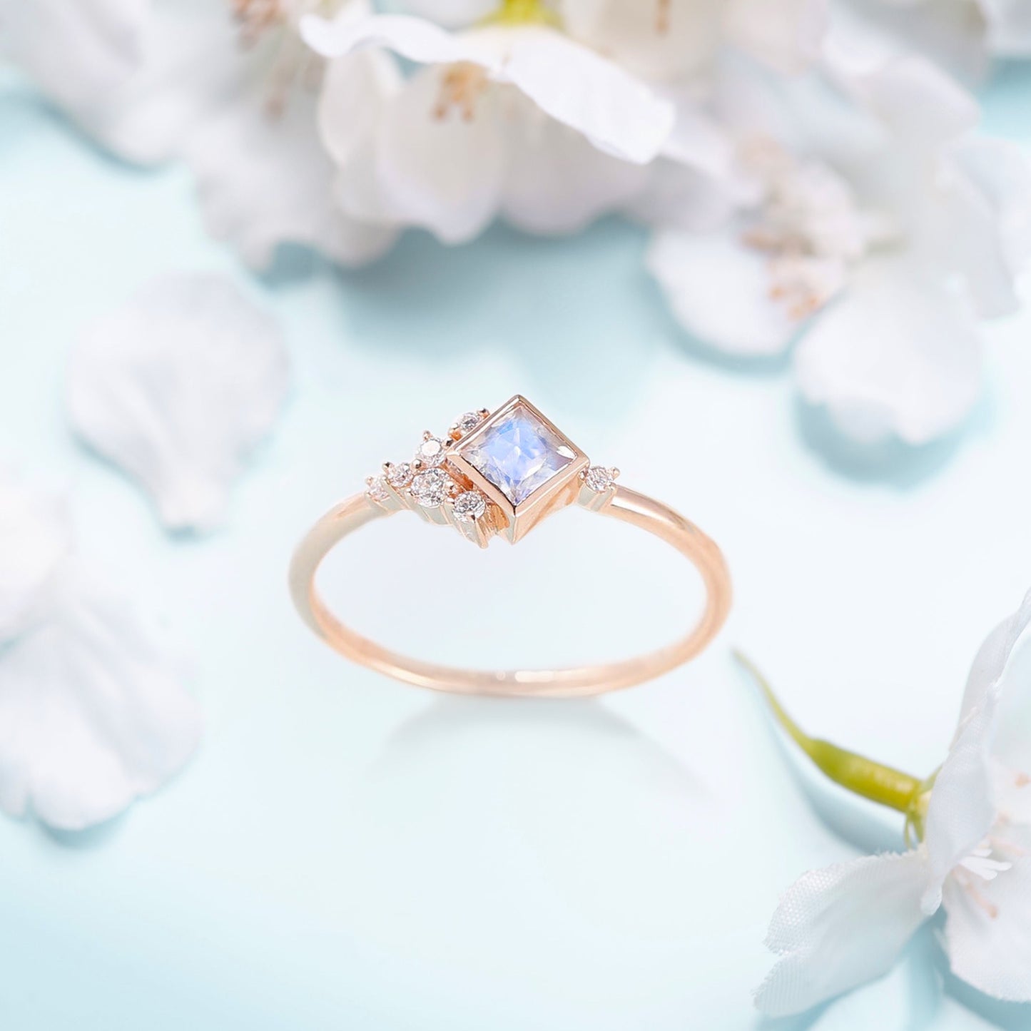 Engagement ring with a Moonstone and white Zircon on a table with flowers