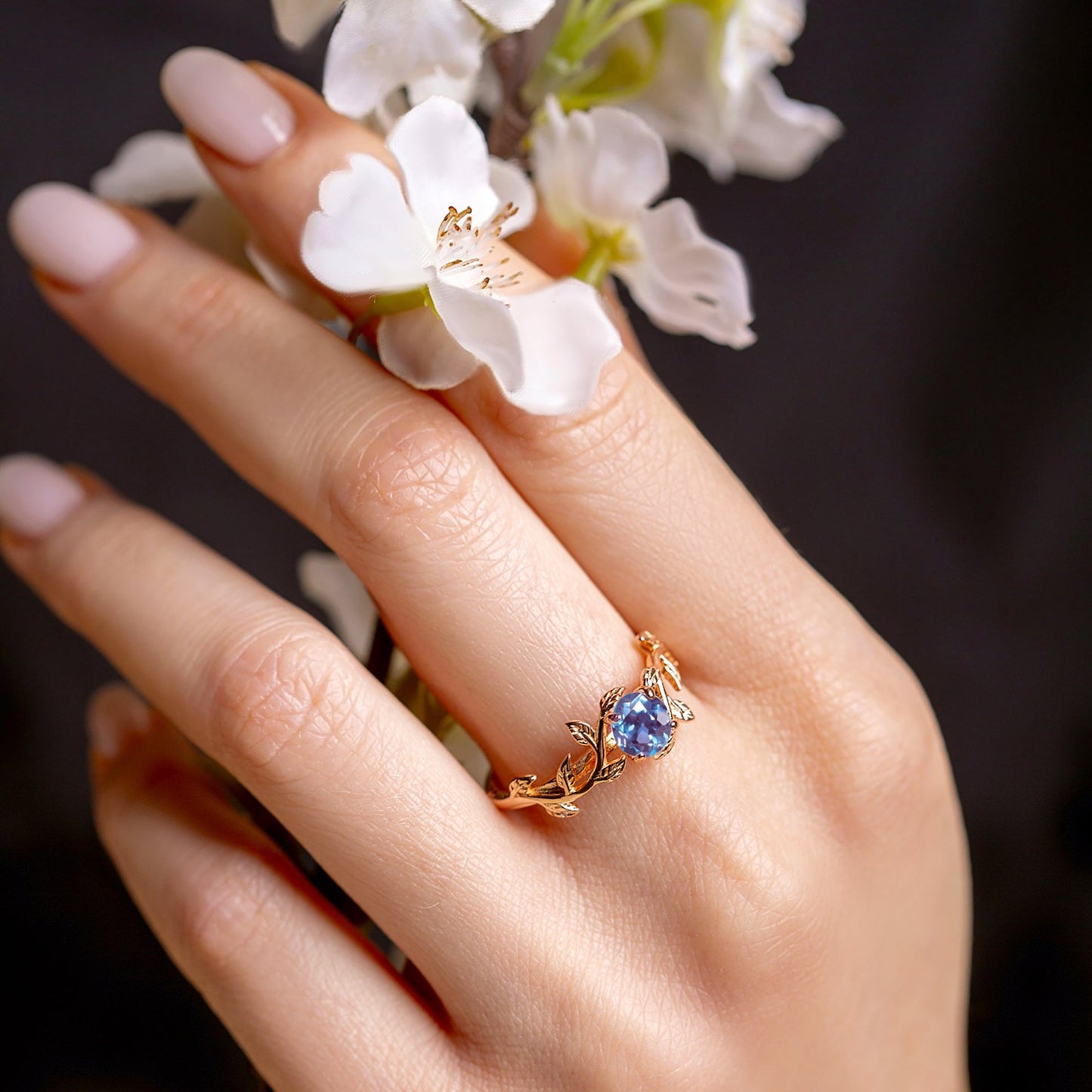 Ring with a blue alexandrite stone on a tender woman hand, which holds flowers
