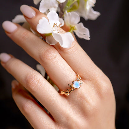 Ring with a moonstone in a twig form on a woman hand, which holds flowers