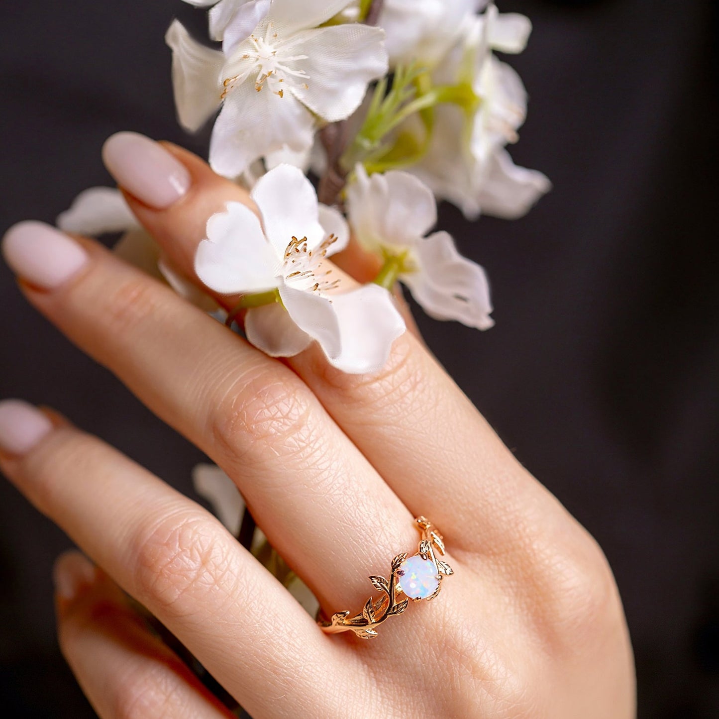 Ring with a twig form and white opal on a woman hand, which holds flowers